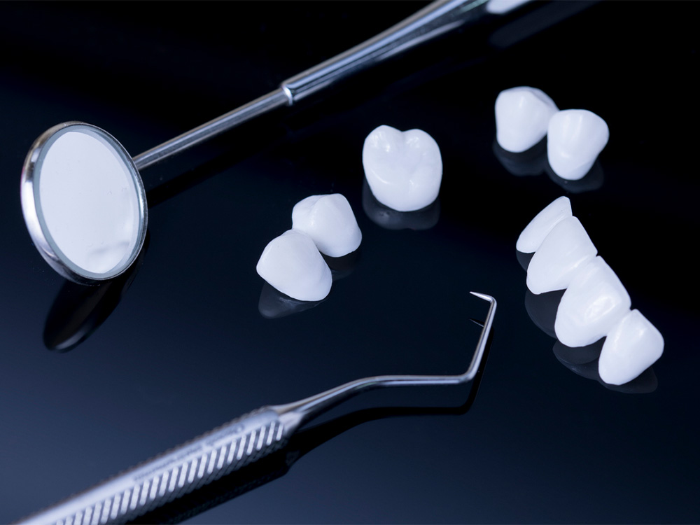 dental crowns and bridges along with dental exam instruments on a dark background