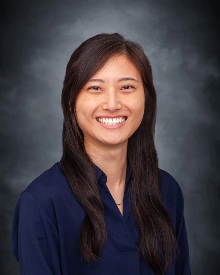 Dr. Jane Lee with long dark hair wearing a dark blue shirt against a dark gray gradient background. The scene appears professional and formal, without any accompanying text or elements.